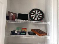 Middle and lower shelves with various boxed board games including Cards Against Humanity and a wooden chess/checkers set, as well as game boxes in green and orange covers.