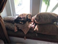 Photo of stacked pillows, throws, and valences on a window seat with natural light.