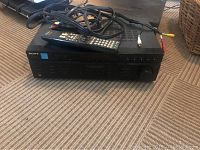 Front and side view of the black Sony digital amplifier with remote control and cables on a carpeted floor.