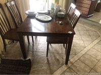 Wood kitchen dining table with brown finish and some surface scratches. Four matching chairs around the table with vertical slats.