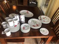 Wide shot of porcelain dinnerware set with floral watercolor pattern on dark wood table.