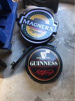 Top-down photo of Magners and Guinness pub signs placed on concrete floor, showing full logos and mounting hardware.