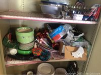 Shelves hold a mix of paper party supplies including rolled paper plates, folded decorations, plastic items, and some metal trays and scoops