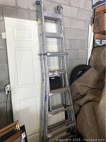 Full view of Werner aluminum extension ladder leaning against a wall and door beside other items in storage.