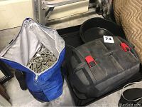 Lot containing two black plastic saw oil pans and a large blue zippered bag of heavy metal chains, all placed on a black surface.