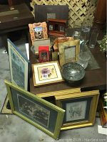 Assorted framed pictures, decorative glass bowls, vases, jars, and wood decor items arranged on dark wood table.