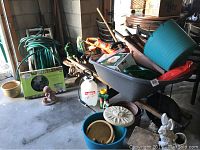 Full view of assorted garden and yard supplies including the gray wheelbarrow filled with items, garden hose on reel, and several yard ornaments on ground.