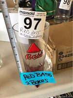Side view of a Red Bass triangle branded glass next to a ruler showing approximate height and two boxes behind it.