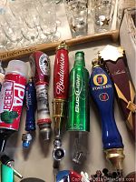 Photo showing a variety of beer tap handles lined up horizontally including Budweiser, Bud Light, Foster's, Rebel IPA, Michelob AmberBock