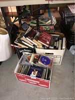 Photo of a cardboard box containing a collection of fiction and cooking books along with DVDs in plastic cases.