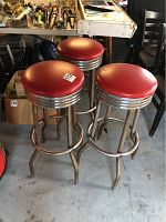 Three red and chrome bar stools with round seats and rusted legs shown from one angle.