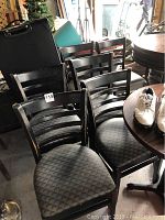 Eight black wooden pub chairs grouped together showing the ladder-style backs and patterned vinyl seats.