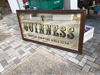 Full view of large Guinness bar picture featuring glass mirror with brand name and harp logo, solid wood frame against outdoor background