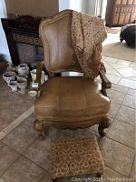 Full front view of tan leather armchair draped with patterned throw, showing seat cushion and carved wooden legs