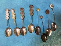 Overview of all 8 Asian collector spoons with varied decorative handles and signs of wear