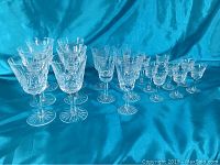 Full view of 19 crystal glasses set on blue fabric showing different sizes and patterns.