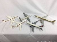 Five model airplanes arranged on white fabric showing different airlines and conditions, some with missing parts.
