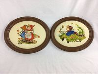Photo showing two Hummel needlepoints in dark brown oval wooden frames, displayed side by side.