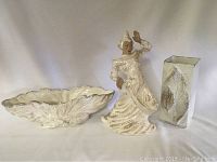 Three white and gold Gilner pottery pieces: a scalloped bowl, a dancing figurine, and a rectangular vase with textured leaf patterns