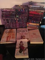 Stack of multiple Harlequin romance novels with additional fiction titles piled vertically and horizontally on a table.