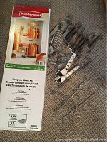 Photo showing Rubbermaid Complete Closet Kit box alongside various metal storage racks and hooks for doors and walls, including wire baskets and compartments.
