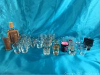 Wide view of over 30 assorted shot glasses in various designs and sizes on blue cloth background showing diversity of the collection.