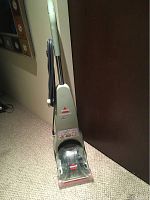 Front view of Bissell Quicksteamer carpet cleaner showing the upright handle, clear cleaning solution tank, and Bissell logos at the base and tank.
