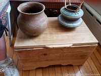 Top view of two clay pots resting on the closed wooden box on a wooden floor.