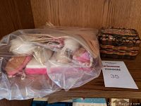 Collection of various antique baby shoes in plastic bag next to a small woven wicker box with lid.