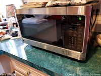 Front and side view of LG tabletop microwave oven on green countertop showing digital touch control panel and stainless steel body.