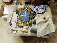 Plastic bin filled with assorted linens including pot holders, kitchen towels, and small blankets or throws.