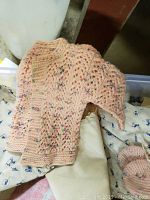 Peach knitted baby bonnet with an intricate openwork pattern.