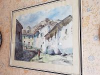 Framed Bolivian watercolor painting showing whitewashed houses, mountains, and a small figure in the street