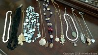 Photo displaying nine different necklaces laid flat on a dark wooden surface.