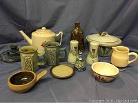 Photo showing miscellaneous pottery items including Buchan Thistleware Portobello Stoneware round lidded casserole, matching salt and pepper shakers, teapot, mugs, small bowls, and bottle.