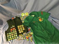 Full view of vintage green Girl Scout dress uniform and dark green vest with many patches and pins scattered around