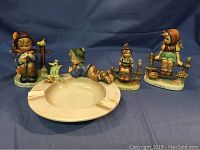 Four Hummel figurines and an ashtray displayed against a blue backdrop, showing all items in the set.