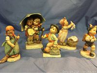 Full set of five vintage Hummel porcelain figurines arranged in a line on a blue backdrop