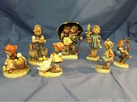 Seven vintage Hummel figurines depicting children in various scenes with some visible wear and chips.