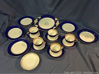 Full set of 17 pieces including cups, saucers, small plates, and serving platter displayed on blue fabric background.