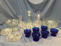 View of the full glass and crystal lot including decanters, clear pressed glass bowls and plates, cordial glasses, and blue dessert dishes on a blue cloth.