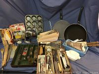 Overview of assorted kitchen items including a muffin tin, silverware trays, wooden spoons, skillet, microwave omelette cooker box