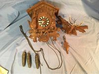 Full view of the cuckoo clock showing the clock face, pinecone weights, chains, and detached carved deer head and pendulum pieces laid out on fabric.