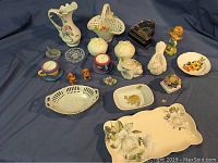 Photo of assorted ceramic and porcelain knick knacks, trays and figurines on blue fabric background