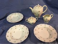 Entire set including teapot, cream, sugar bowl, and three plates arranged on blue cloth.
