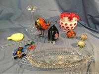 Overview of glass art collection showing cranberry Fenton vase with white coin dot pattern, assorted glass candies, black floral glass egg paperweight signed Violet, small glass bird figurine, small glass floral paperweights, clear Heisey glass relish tray and glass candlestick holder.