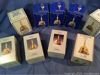 Eight boxed collectible Hummel porcelain bells displayed on a fabric background, showing original packaging and logos.