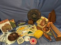 Overview of assorted kitchen accessories and decor items on blue cloth background including wooden bowls, fabric doilies, a green tin container, and various small decorative pieces.