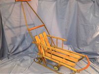Side and front angle view of the vintage children's push sleigh showing overall structure, wooden slats, metal runners, and small wheels.
