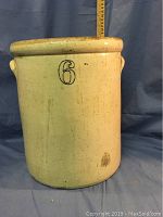 Front view of the 6 gallon crock showing the large cobalt blue number 6 on the beige exterior. Height indicated by measuring stick behind it is about 15 inches.